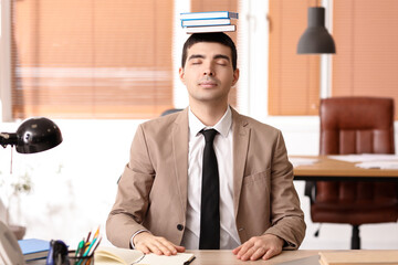 Young businessman with books meditating in office. Balance concept