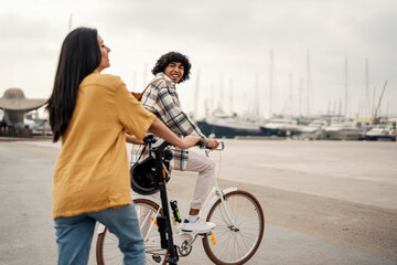 A cheerful tourist couple in love is riding a bike and electric scooter on a dock.