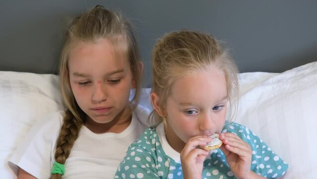 Children, sisters, watch cartoons and eat goodies, cookies. Close up on portrait of two girls hugging and watching TV.