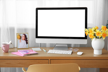 Comfortable workplace with modern PC and narcissus flowers near window