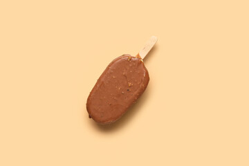 Delicious chocolate covered ice cream on stick against beige background