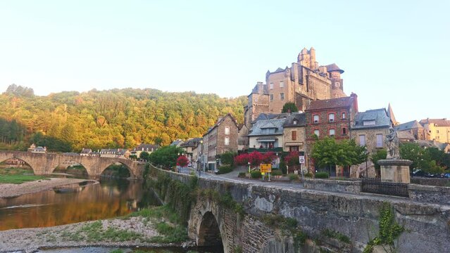 Summer view of scenic French township of Estaing on bank of Lot River overlooking medieval stone arched bridge and fortified castle towering above residential buildings. High quality 4k footage