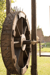ANCIENT WOODEN WHEEL ON BACKGROUND OF GARDEN AND ANCIENT CASTLE