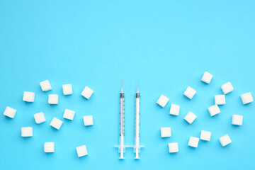 Sugar cubes with syringes for insulin injection on blue background