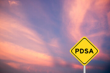 Yellow transportation sign with word PDSA (Abbreviation of plan do study act) on violet color sky...