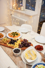Festive celebration table decorated with white and golden tablecloth, with salad assortment, cheese platter, smoked salmon, wine glasses, bokeh lights