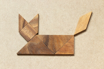 Wooden tangram in cat sitting or lying shape on wood background