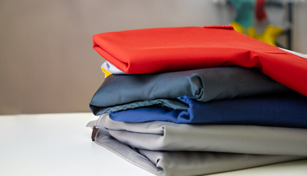 stack of clothes, stack of colorful clothes, White table , blue, red, yellow, white, gray, brown, black, unstitched fabrics clothes top on table, Blurred white background, Ai Generate 