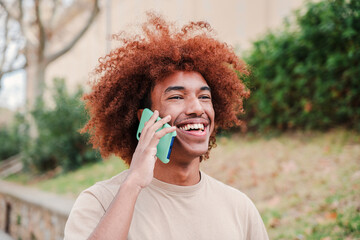 Young african american guy smiling having a mobile phone call outdoors. Happy teenager with toothy smile talking by cellphone. Youngster man laughing on a friendly smartphone conversation at campus