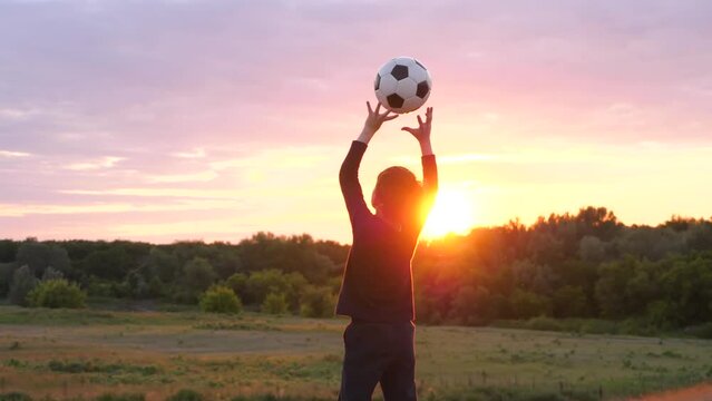A child throws a ball up against the background of the sunset. Silhouette of a child playing outdoors. kids dreams, children in sports