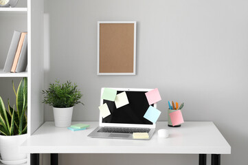 Modern workplace with laptop, sticky notes and board near white wall