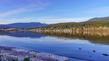 Reflections on tranquil waters of Burrard Inlet, Port Moody, BC, Canada, with mountain backdrop.