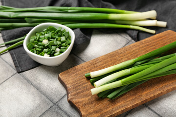 Wooden board and bowl with fresh green onion on dark tile background