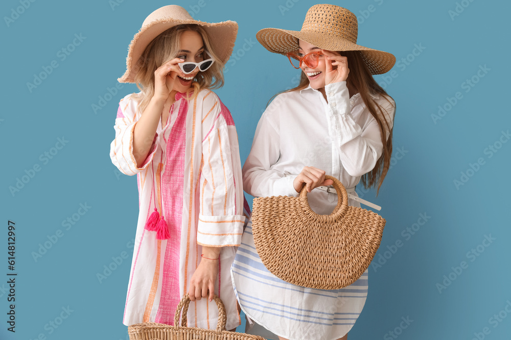 Wall mural young sisters in summer hats and sunglasses on blue background