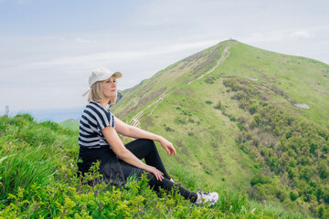 Naklejka na ściany i meble blond tourist woman in her forties in sportswear sits on a high mountain, rests and enjoys the view of nature during a hike