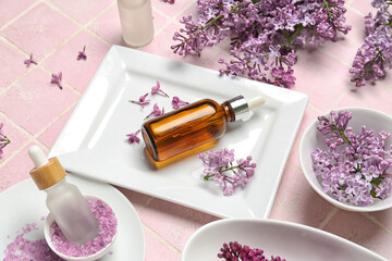 Fototapeta na wymiar Bottles of lilac essential oil, sea salt and flowers on pink background, closeup
