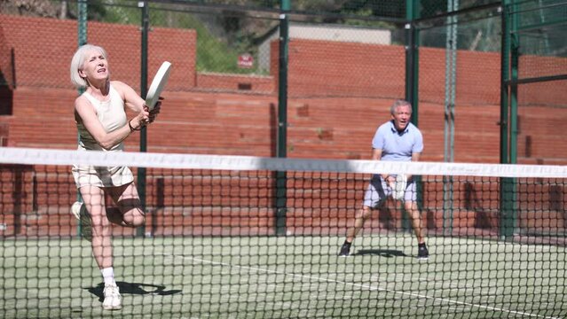 Active aged woman practicing Padel Tennis with other players in the tennis court outdoors