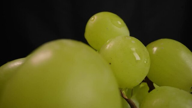 Grapes on a black background. Ripe juicy grapes rotate on a plate. Close-up of a bunch of white grapes. A fresh bunch of juicy grapes rotates on a black background. Grapes close-up rotates.