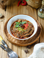 Tumis Daging Sapi Mercon or Stir fry or saute of beef with onion, red cayenne pepper and other herb and seasoning. Serving in white plate on wooden table. Indonesian food, recipe and cuisine