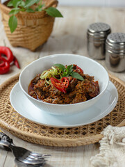Tumis Daging Sapi Mercon or Stir fry or saute of beef with onion, red cayenne pepper and other herb and seasoning. Serving in white plate on wooden table. Indonesian food, recipe and cuisine
