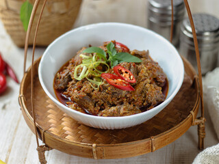 Tumis Daging Sapi Mercon or Stir fry or saute of beef with onion, red cayenne pepper and other herb and seasoning. Serving in white plate on wooden table. Indonesian food, recipe and cuisine