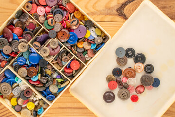 Many buttons in a plastic container on a wooden table, macro, top view.