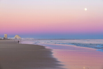 Almost empty beach at sunset, with the full moon in the sky