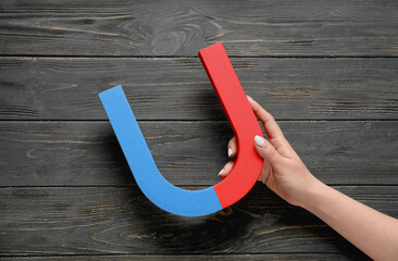 Female hand with magnet on dark wooden background