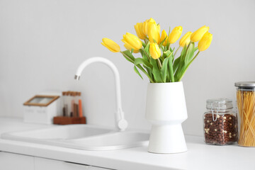 Vase with yellow tulip flowers on countertop near kitchen sink
