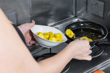 close-up of the hands of a woman taking fried plantains out of the frying pan to make patacones