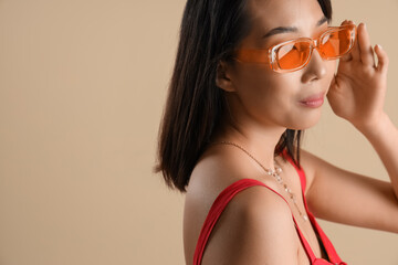 Beautiful Asian woman in stylish sunglasses on beige background, closeup