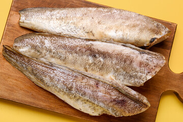 Wooden board with raw codfish on yellow background