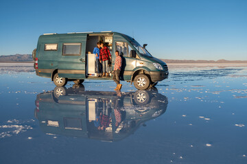A family in a 4x4 camper van in a salt flat with water that generates a perfect reflection