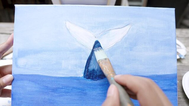 Painter's hand is holding brush to paint a beautiful dolphin painting. Learn to paint in your free time. paint on white cloth with the intention of creating beautiful images as intended by art school