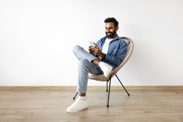 Arabic Man Texting On Cell Phone Sitting In Armchair Indoor