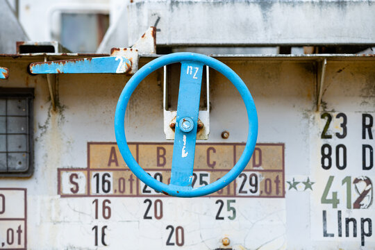 Blue hand wheel for the brakes of a freight wagon. Close up of  old weathered steel parts of an abandoned railway vehicle with flaking off white paint. Technical data typography in the background.