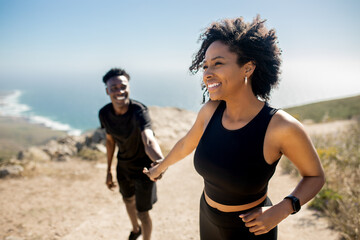 Happy black lady leading man by hand on rocks near ocean, enjoy break from morning workout outdoors