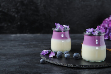 Glasses of panna cotta with blueberry and beautiful hydrangea flowers on black table