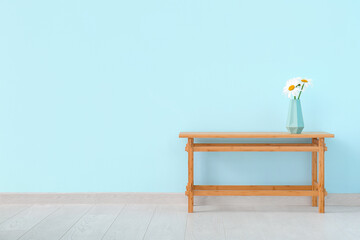 Wooden table with blooming daisy flowers in vase near blue wall