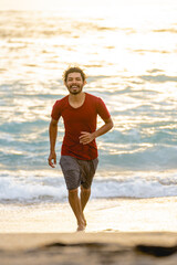 Fototapeta na wymiar Vertical image of a smiling young man running through the waves at the shore of the beach on a summer day with beautiful sunset light.