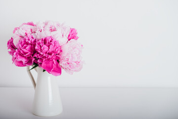 Beautiful bunch of fresh peonies in full bloom in vase against white background. Copy space for text. Minimalist floral still life with blooming flowers.