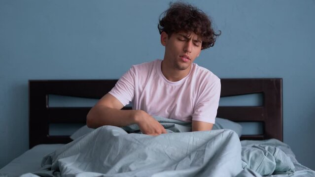 Sleepy guy lying in bed. Hard to wake up early in morning. Man does not get enough sleep.