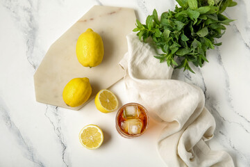 Glass of ice tea and board with lemons on white background