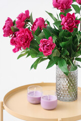 Vase with red peonies and candles on coffee table near white wall