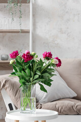 Vase with red peonies, couch and shelving unit in living room