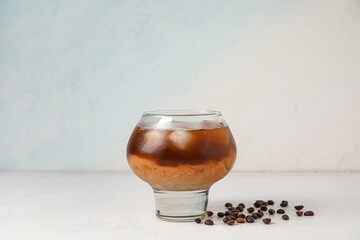 Glass of tasty ice coffee with milk on light background
