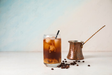 Glass of tasty ice coffee with milk and cezve on light background