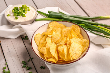 Bowl of tasty sour cream with sliced green onion and potato chips on grey wooden background