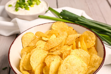 Bowl of tasty sour cream with sliced green onion and potato chips on grey wooden background