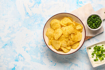 Bowls of tasty sour cream with sliced green onion and potato chips on blue background
